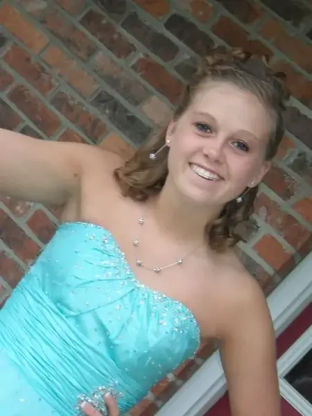Tori, smiling, in a pale blue formal dress in front of a brick wall