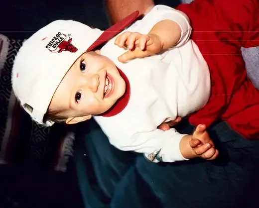 A baby laughing in an oversized ball cap
