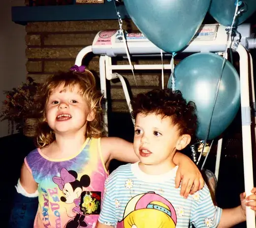 Two small children side by side under teal balloons