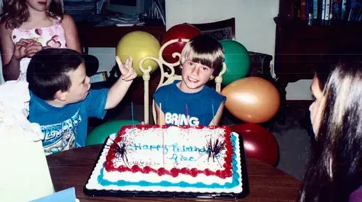 Two boys behind a birthday cake, balloons waiting
